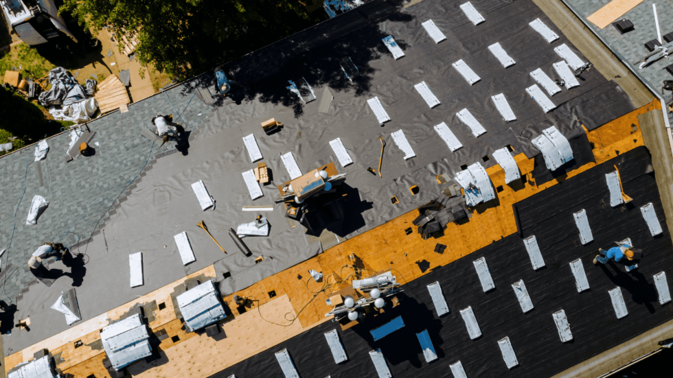 Multiple roofers work to construct a large roof that is covered in roofing materials 980x551