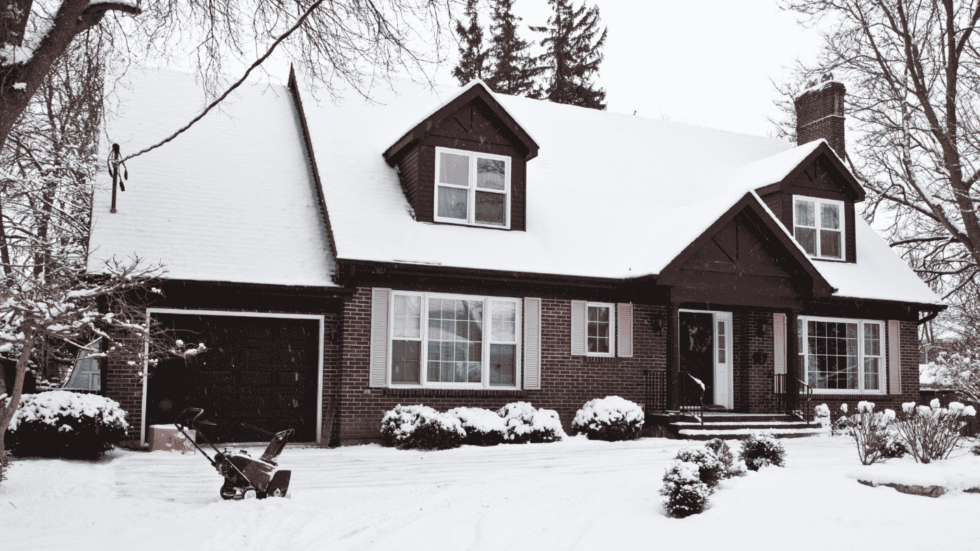 A brick house blanketed in snow which covers the front yard and roof 980x551