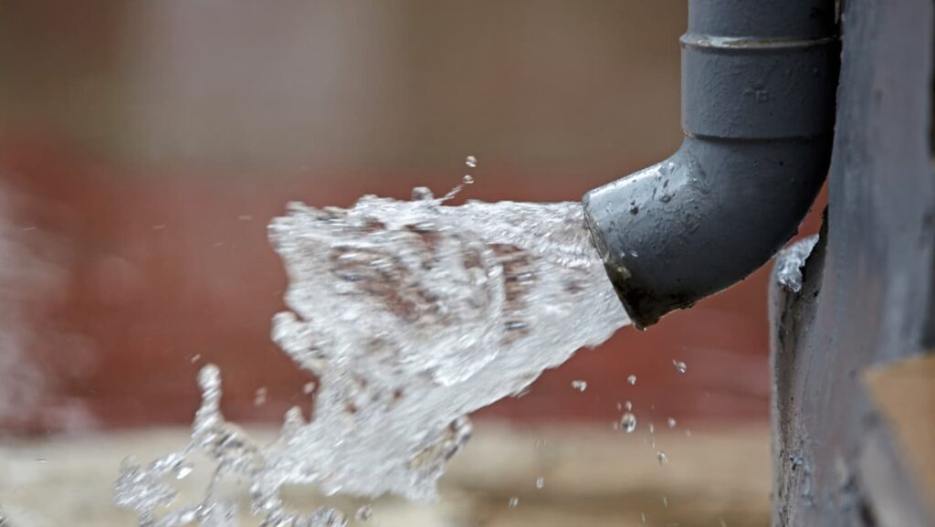 A round, grey downspout erupts with water.