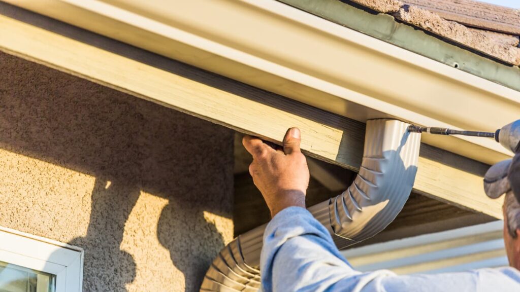A professional installs new gutters on a roof.