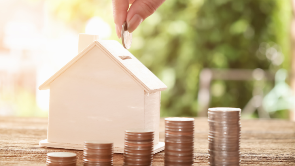 A wooden piggybank shaped like a house with piles of coins.