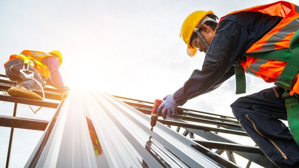 Two roofers work to install metal roofing on a commercial building.