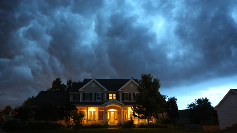 A home with porch lights on under a dark, stormy sky.
