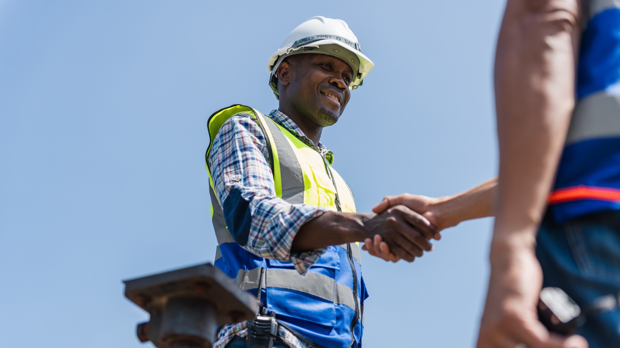 A roofing construction mentor shakes hands with their new apprentice at a job site.